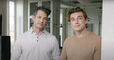 Nate Berkus and Jeramiah Brent, two white men with short brown hair, standing in front of a mirrored wall in their Fifth Avenue home.