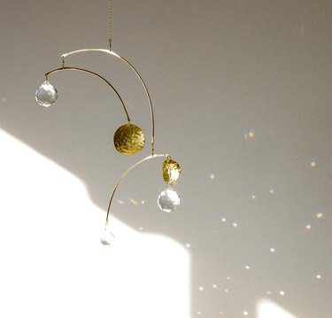 A prism made of gold wire and clear crystals that reflect rainbows on the white wall.