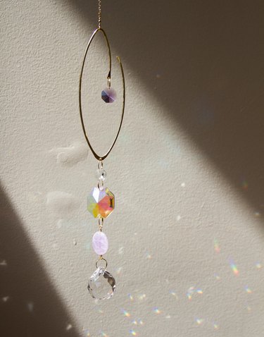 A mobile made of gold wire and light pink, purple, rainbow, and clear crystals that reflect rainbows on the wall.