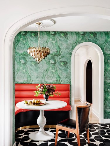 A dining room with red bench, green walls, and black patterned floors