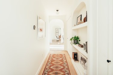 Hallway with built-in shelves, kilim rug, ceiling right, arched doorway, arched bookshelves.