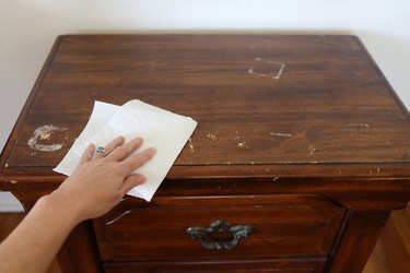 Wiping old nightstand clean with a paper towel