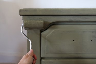 Painting the nightstand olive green with a small paint roller