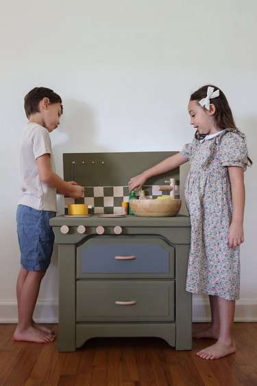 Two small children playing with a green play kitchen