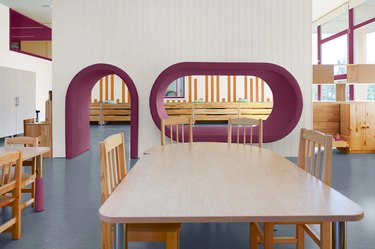 A wooden kitchen table with four chairs in front of a white wall with dark purple accents in the doorway and window.