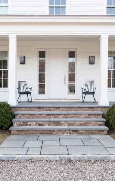 Farmhouse with white door, white exterior and trim, rocking chairs.