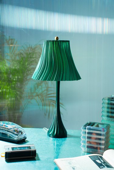 A green 3D-printed wavy lamp on a light blue desk.
