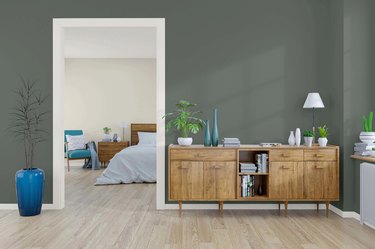 Wooden dresser in front of a dark green-gray wall with a doorway leading into a bedroom