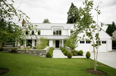 White farmhouse with front lawn, boxwood, trees.