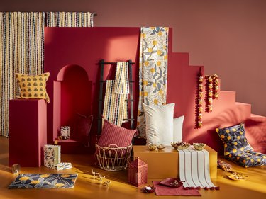 Burnt red walls and orange flooring topped with pillows, baskets, and towels with a rainbow curtain in the background.