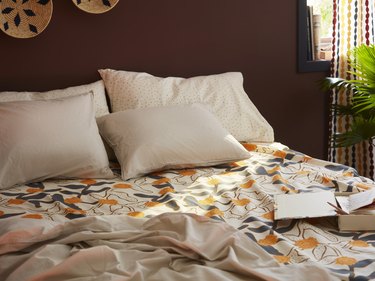 Orange floral bedding with cream pillows in front of a wooden headboard.