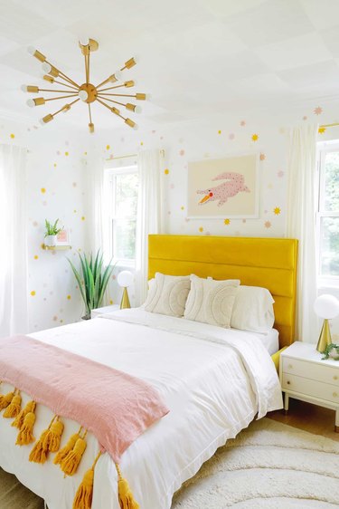 A white room with polka dot spots on the wall and a yellow headboard.