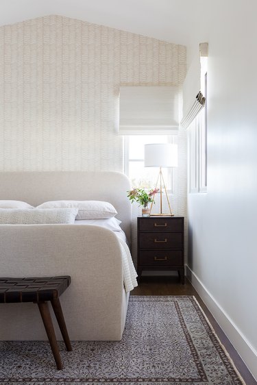 A white bedroom with cream bed frame with darker nightstand and bench.