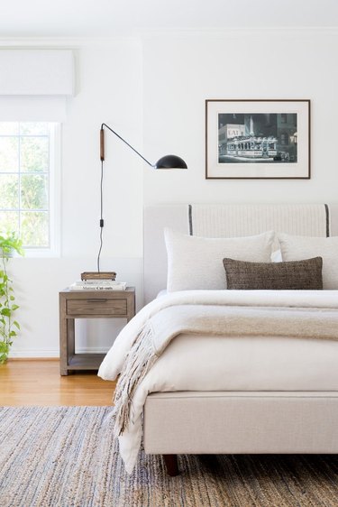 White bedroom with gray rug, lumbar pillow, and nightstand.