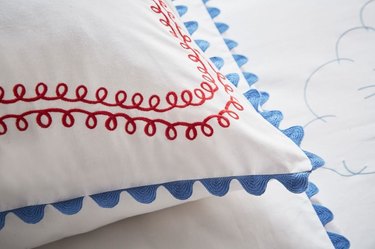 A white Peter Reed pillow with red swirly lives on it and wavy blue edging.