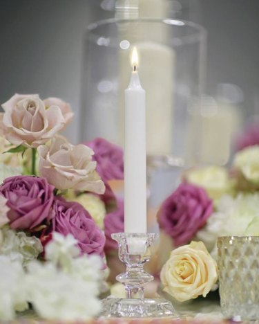 A white Price's Candles Sherwood tapered candle on a table with pink and purple roses.