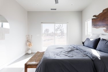 Bed, bench, vase, dried flowers, mirror, sliding glass door.