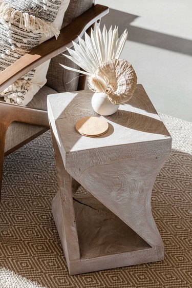 End table with dried flowers, rug, pillow.