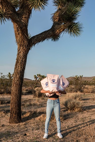 Woman holding bags of coffee near a Joshua tree.