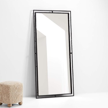 Black floor mirror resting against a white wall
