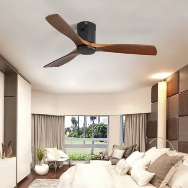 A brown low-profile ceiling fan with three blades in a white bedroom.