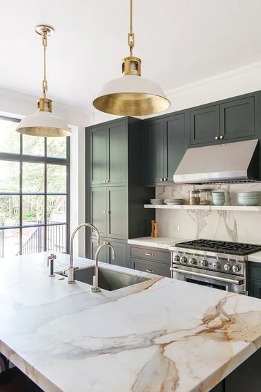 Kitchen with dark green cabinets, stainless steel appliances, and marble countertops.