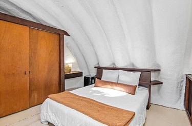 White bed with brown accents next to a wooden closet underneath white arched ceilings