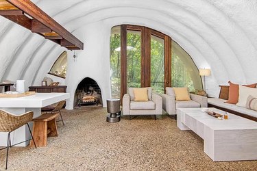 Living room with white arched ceilings and tan accents. There is a fireplace in the corner and a partially-visible white kitchen.