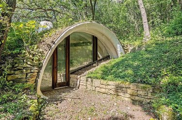 Exterior of a hobbit house building into greenery with an arched doorway.