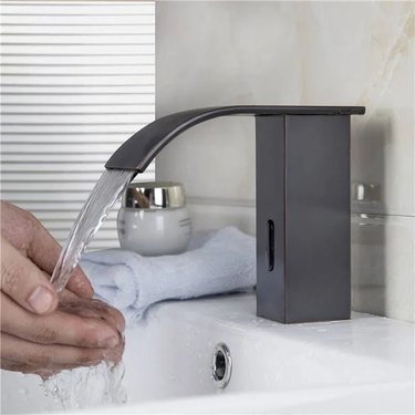 A person washes their hands using a touchless faucet in the bathroom