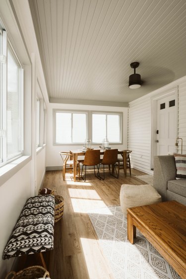 Sunroom with gray shiplap painted ceiling, light wood floors and black ceiling fan.