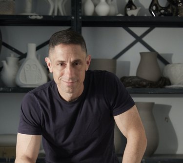 Jonathan Adler in a black shirt in front of a shelf of pottery