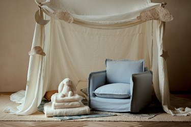 The mini Sixpenny Neva chair in a light blue underneath a fort made from a beige sheet pinned with paper clouds, a star, and a moon.