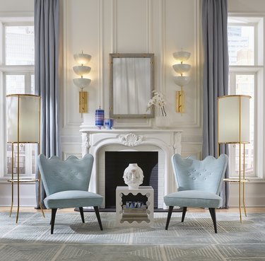 Jonathan Adler wavy accent table in a room with two light blue chairs, a fireplace, a mirror, lights, and white and gray accents