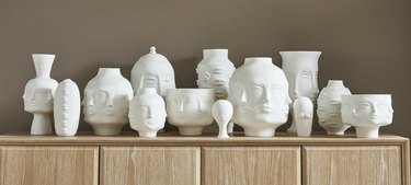 Jonathan Adler Muse collection showcasing white ceramics shaped as different faces on a wooden console