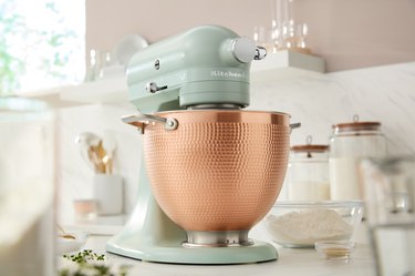 KitchenAid Blossom stand mixer in a soft green with a bronze bowl on a white countertop.
