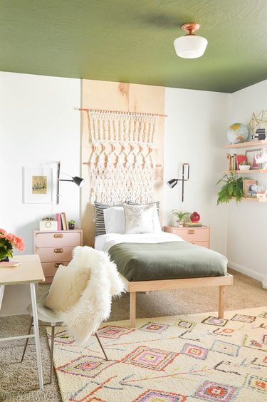 Bedroom with green painted ceiling, macrame wall hanging and black wall sconces.