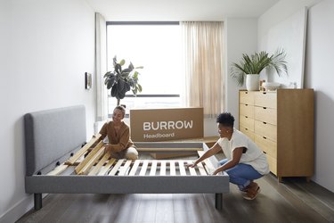 Two people assembling the Burrow gray fabric bed frame.