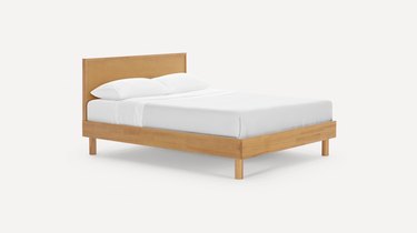 Burrow bed frame and headboard in an oak finish with a white mattress and pillows on top.