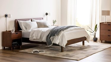The Burrow Chorus Bed frame in a dark oak in a bedroom covered in white linens.