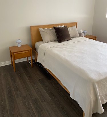 The oak Burrow Chorus bed frame in a bedroom topped with light blue linens and surrounded by walnut nightstands on both sides.