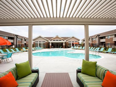 Apartment complex surrounded by a pool with couches and lounge chairs.