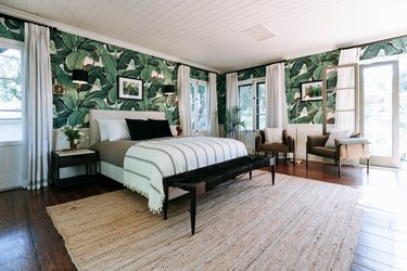 A bedroom with palm leaf wallpaper and floor length drapes