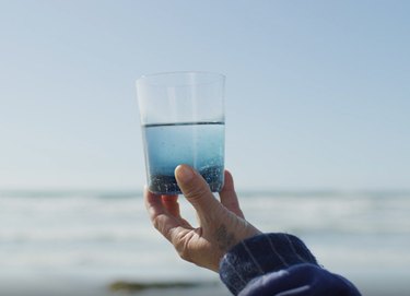 person holding glass with water with ocean in the background