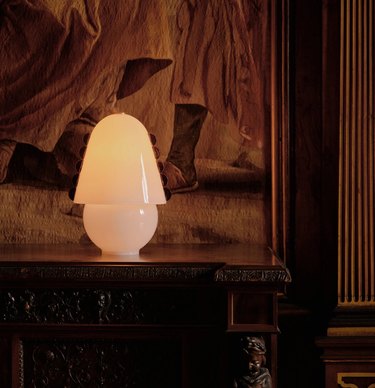 White table lamp with a curved top on a wooden table in front of an old painting