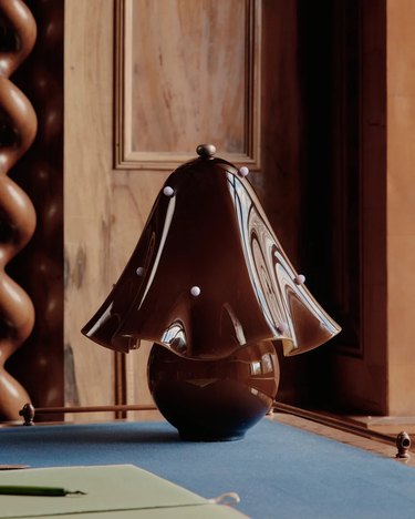 A brown, wavy table lamp on a blue surface in front of a wooden wall