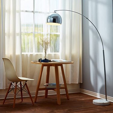chrome arc lamp over wood table with white eames-inspired chair