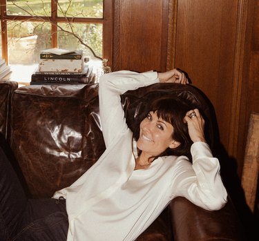 Designer Leanne Ford, a person who short brown hair, on a brown leather sofa, wearing a white button-down shirt.