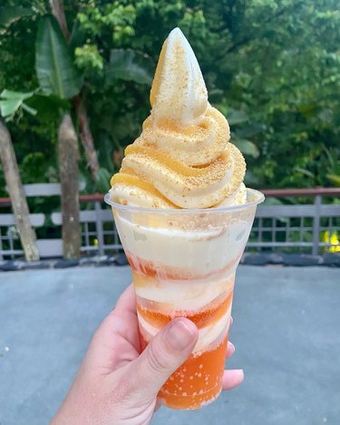 A hand holding up an orange Dole Whip float covered in orange Fanta and graham cracker crumbs.
