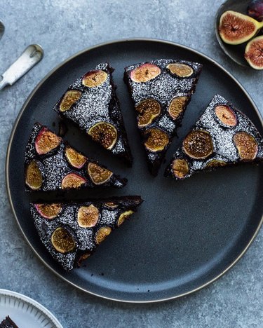 Five pieces of chocolate and honey fig cake on a black plate taken from above over a table.